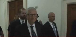 Bill Gates betrapt op een grijns terwijl hij een besloten Epstein-hoorzitting binnengaat, afgeschermd van het publiek